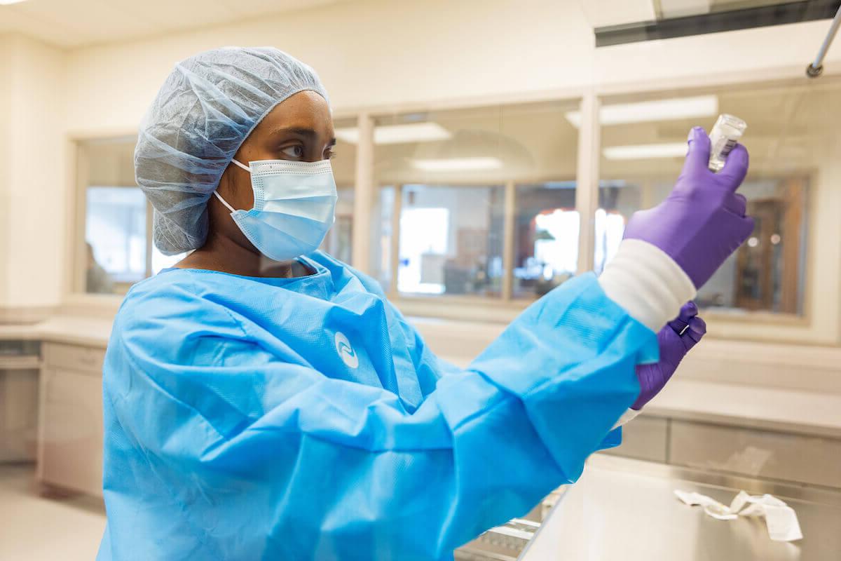 Shenandoah University Bernard J. Dunn School of Pharmacy student in blue scrubs, gloves, cap and mask, holding a vial.